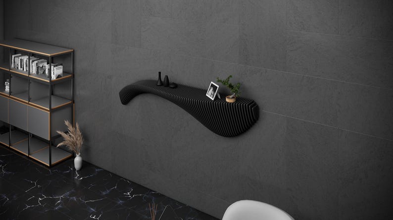 May include: A black, wavy, wall-mounted shelf with a small potted plant, a picture frame, and three small decorative objects on top.