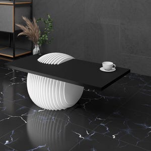 May include: A black coffee table with a white, round, layered base. A white cup and saucer are on the table.