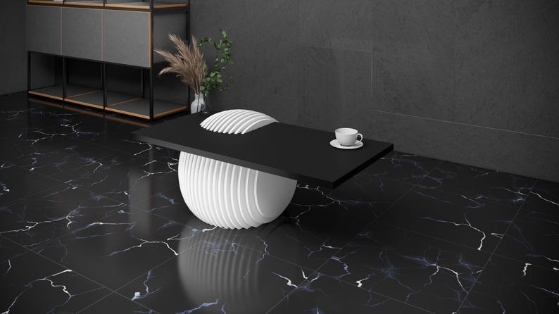 May include: A black coffee table with a white, round, layered base. A white cup and saucer are on the table.