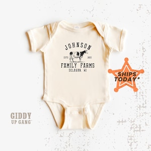 May include: A cream-colored baby onesie with a black and white cow illustration and the text "Johnson Family Farms, Delavan, WI, Est. 2025".