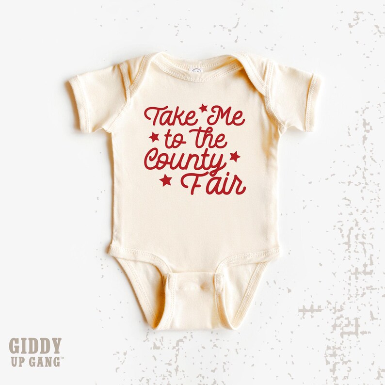 May include: A cream-colored baby onesie with red text that reads "Take Me to the County Fair" with red stars.