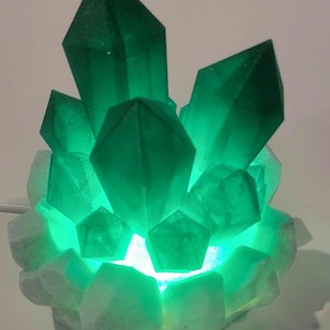 May include: A green crystal lamp with a white base. The lamp is lit and the light shines through the crystals.