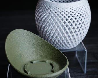 May include: A white, lattice-patterned decorative vase and an olive green, oval-shaped planter. The vase has a spherical shape with a diamond-shaped pattern. The planter has a textured surface and a circular base.