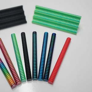 May include: Assortment of ten colorful, textured, plastic rods. The rods are arranged in a semi-circle on a white surface. Two green, textured, plastic rectangles are also visible in the background.