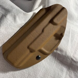 May include: A brown leather holster for a handgun. The holster has a snap closure and is designed to be worn on the belt.