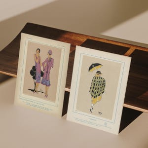 May include: Two vintage fashion illustrations. One features two women in purple dresses, the other shows a woman in a yellow dress and a black and yellow checkered coat holding a black umbrella. The illustrations are on aged paper.