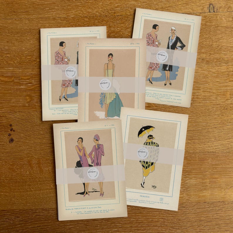 May include: A collection of vintage fashion illustrations, featuring women in stylish attire. The illustrations are in soft pastel colors, with a focus on elegant dresses and accessories. The prints are held together with a white band.