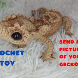Könnte beinhalten: Gehäkeltes Gecko-Spielzeug in Braun- und Tan-Farben. Der Gecko hat große schwarze Augen und eine strukturierte Oberfläche.
