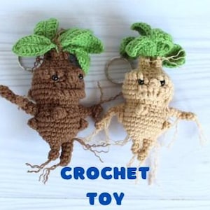 Pode incluir: Dois chaveiros de Mandrágora de crochê. Um é marrom, o outro bege, ambos com folhas verdes e pequenos olhos pretos. Os chaveiros são feitos à mão e apresentam raízes e braços pendurados. A palavra "CROCHET TOY" está escrita em azul.