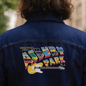 May include: Dark blue denim jacket with a colorful "Greetings from Asbury Park N.J." graphic on the back. The graphic features a yellow guitar and text in red, blue, green, and yellow.