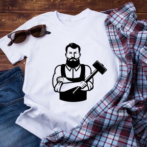 May include: White t-shirt with a black and white illustration of a bearded man holding a hammer.
