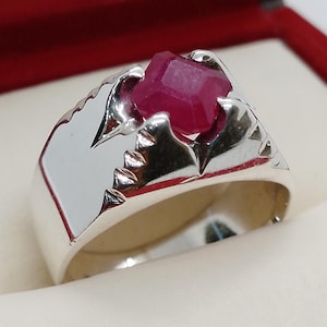 May include: A silver ring with a red gemstone set in a claw setting. The ring has a textured band.