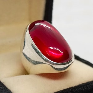 May include: A silver ring with a large, oval-shaped, bright red gemstone.