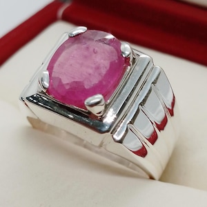 May include: A silver ring featuring a large, pink gemstone set in the centre. The ring has a wide band with a textured design.