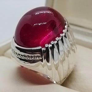 Peut inclure: Une bague en argent avec une grande pierre précieuse ronde de couleur rouge foncé.