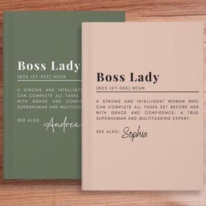 May include: Two green and pink hardcover journals with the text "Boss Lady" and the definition of the word. The green journal has the name "Andrea" written below the definition. The pink journal has the name "Sophia" written below the definition.
