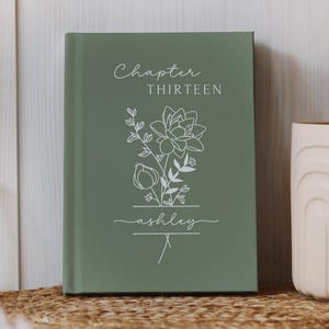 May include: A white ceramic mug with a black handle and the text "But First, Coffee" in a black, handwritten-style font. The mug is on a white surface.