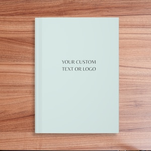 May include: A light blue blank journal with the text "YOUR CUSTOM TEXT OR LOGO" printed in black.