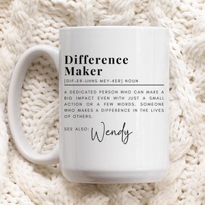 May include: White ceramic coffee mug with black text that reads "Difference Maker [DIF-ER-UHNS MEY-KER] NOUN A DEDICATED PERSON WHO CAN MAKE A BIG IMPACT EVEN WITH JUST A SMALL ACTION OR A FEW WORDS. SOMEONE WHO MAKES A DIFFERENCE IN THE LIVES OF OTHERS. SEE ALSO: Wendy"