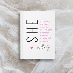 May include: A white card with black text that reads "SHE is creative, is strong, is confident, is intelligent, is blessed, is happy, is beautiful, is enough. ❤ is Emily".