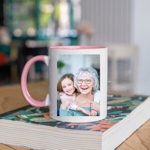 May include: A white ceramic mug with a pink rim and handle. The mug features a photo of an older woman and a young girl smiling at the camera.