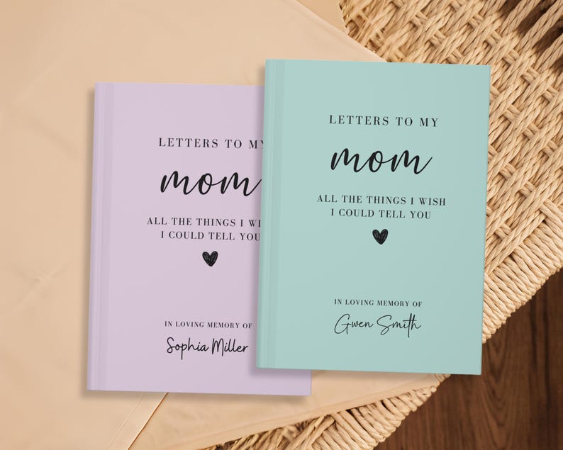 Op de afbeelding: Twee notitieboekjes, een in lavendel en de andere in lichtblauw, met de tekst "Brieven aan mijn moeder" en "Alles wat ik je wil vertellen". De notitieboekjes hebben een zwart hart en de tekst "Ter nagedachtenis aan" gevolgd door een naam.