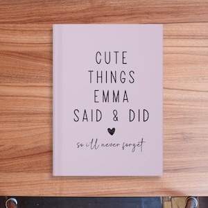 May include: A lavender-colored journal with the text "Cute Things Emma Said & Did so I'll never forget" in black lettering. A small heart symbol is between "Said" and "Did".