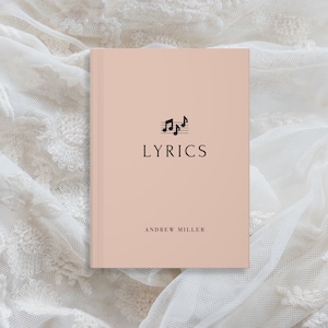 May include: A pink notebook with the word "LYRICS" printed in black on the front cover. The cover also features a black musical note symbol. The author's name, "ANDREW MILLER", is printed in black at the bottom of the cover.