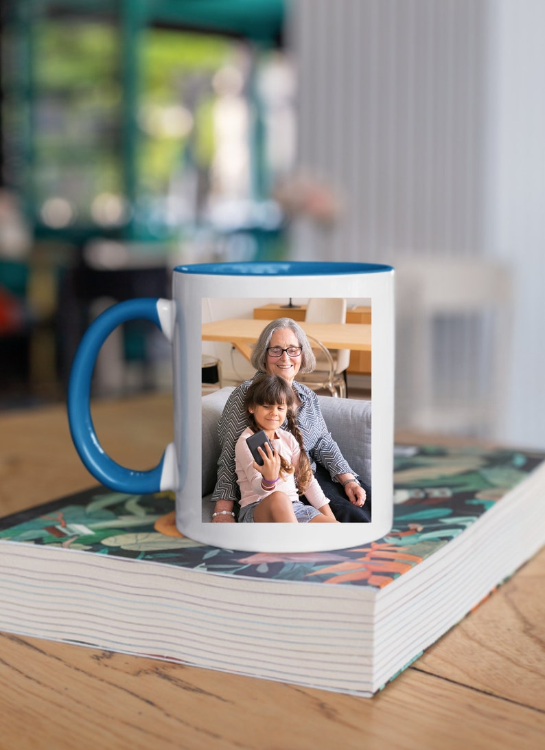 May include: A white ceramic mug with a blue rim and handle. The mug features a photo of an older woman and a young girl smiling at the camera. The photo is printed on the front of the mug.