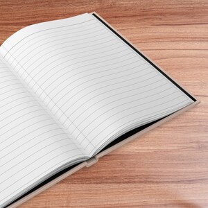 May include: A black and white lined notebook with a black cover is open on a wooden surface.