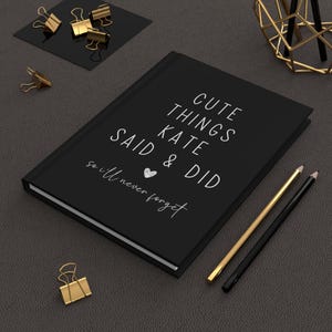 May include: A black journal with the text "Cute things Kate said & did so I'll never forget" in white lettering. A small heart is drawn next to the text.