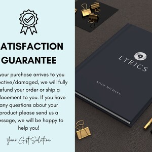 May include: A dark blue notebook with the word "LYRICS" in white text and a white record player icon. The notebook has the name "NOAH MICHAEL" printed in white text. The notebook is on a brown surface with gold paper clips and a black and gold pen.