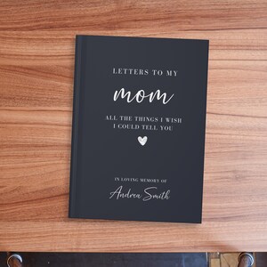 Op de afbeelding: Een zwart dagboek met de tekst "Letters to my mom" en "All the things I wish I could tell you" in witte letters. Het dagboek heeft ook een klein hartje en de tekst "In loving memory of Andrea Smith" in witte letters.