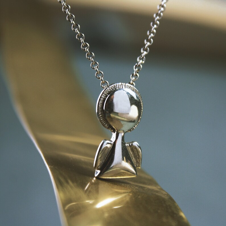 May include: A silver necklace with a small angel pendant. The angel has a round head and small wings.