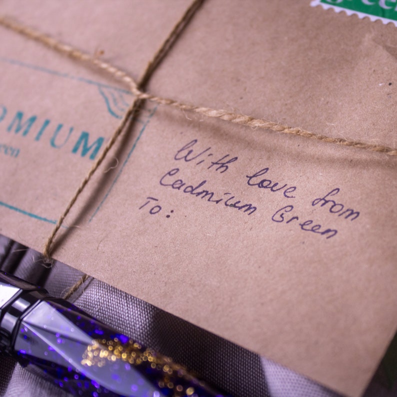 May include: A brown paper package with twine tied around it. The package is addressed with the handwritten message "With love from Cadmium Green" and "To:".