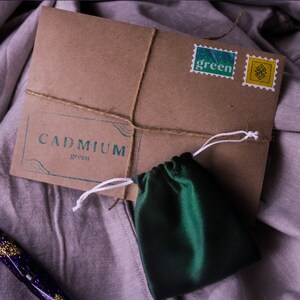 May include: A brown paper envelope with a green pouch and two stamps. The stamps say "green". The envelope has a label that says "CADMIUM green".
