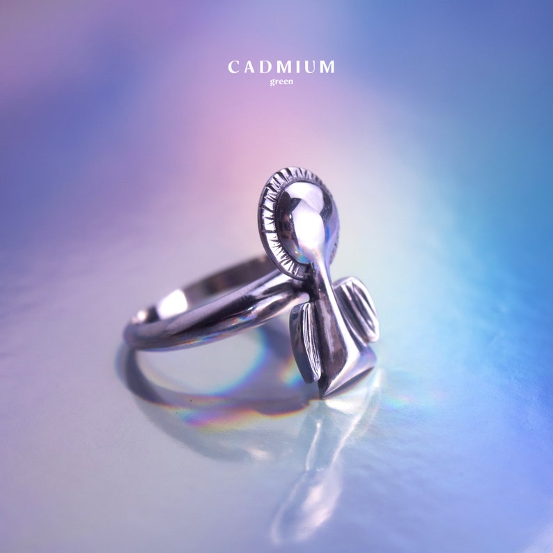 May include: Silver ring with an angel design. The angel has a halo and wings. The ring is on a light blue background.