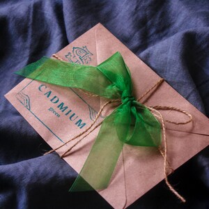 May include: A brown paper envelope with a green ribbon tied around it. The envelope has the words "CADMIUM green" printed on it.