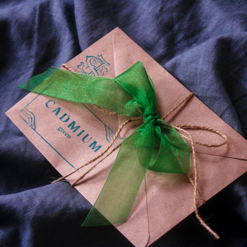 May include: A brown paper envelope with a green ribbon tied around it. The envelope has the words "CADMIUM green" printed on it.