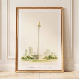May include: A framed watercolour print featuring the National Monument of Jakarta with a gold flame top, surrounded by stylised city buildings and green foliage. The bottom of the print includes the text JAKARTA CITY STUDY 2026 in black font.