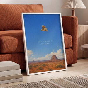 May include: A framed rectangular wall art print featuring a bright blue sky over a desert landscape with rock formations. A small light-colored dog is depicted floating in the sky. The text reads: DON'T OVERTHINK IT, FLY ANYWAY.
