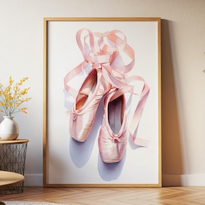 May include: A framed print featuring a pair of pink ballet pointe shoes with long, flowing ribbons. The shoes are set against a white background, with soft shadows adding depth. The artwork is encased in a light brown wooden frame.