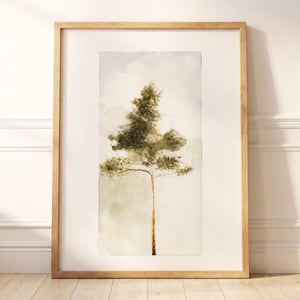 May include: A vertical rectangular framed wall art piece featuring a watercolour painting of a single pine tree. The tree has a slender brown trunk and dark green foliage against a soft, muted beige and light grey background within the frame.