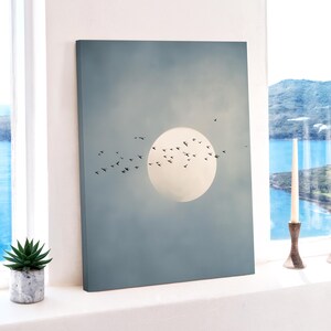 Pu&ograve; includere: Una stampa su tela raffigurante un grande cerchio pallido, simile al sole, su uno sfondo di cielo blu tenue. Uccelli silhouette volano davanti al cerchio. L'opera d'arte &egrave; esposta vicino a una finestra con una piccola pianta succulenta in vaso.