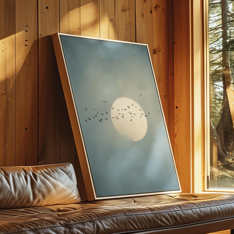 Pu&ograve; includere: Una stampa artistica incorniciata con un paesaggio sereno con un grande sole giallo pallido e uno stormo di uccelli in volo contro un cielo blu-verde attenuato. L'opera d'arte &egrave; esposta su una parete di legno, vicino a una finestra.