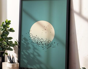 May include: Framed art print featuring a large, cream-colored circle against a teal background. Silhouetted birds fly from the circle. The artwork is in a black frame and rests on a wooden surface, with a plant and pencils in the foreground.