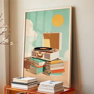 May include: A framed art print featuring a vintage record player atop a stack of books. The artwork has a retro aesthetic with a teal sky, a yellow sun, and white clouds. The record player is white with a brown handle.