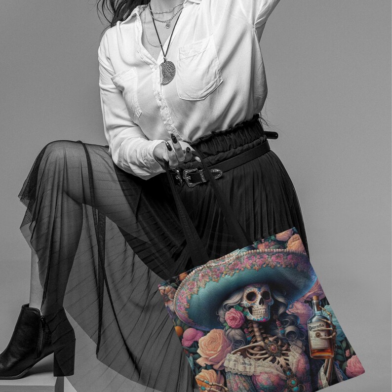 May include: A black tote bag with a colorful design featuring a skeleton wearing a sombrero and holding a bottle of tequila. The design is surrounded by flowers and leaves.