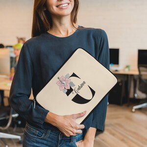May include: A beige laptop sleeve with a black floral design and the name "Cabrina" printed on it.
