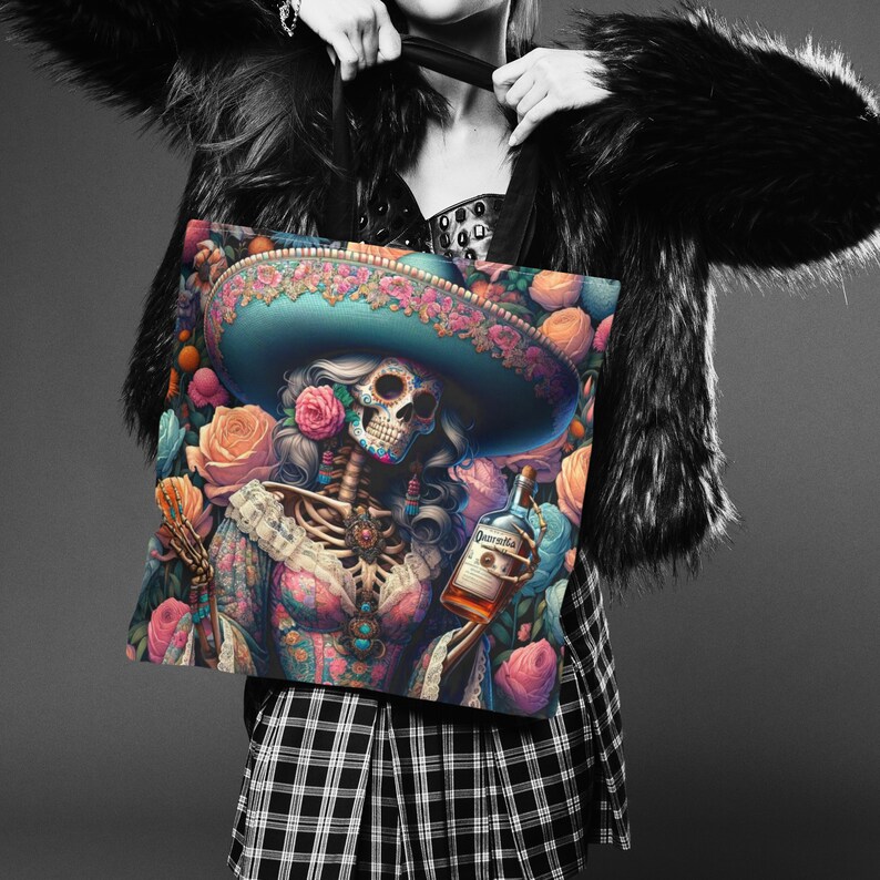 May include: A tote bag featuring a colorful illustration of a skeleton woman wearing a sombrero and holding a bottle of Patron tequila. The background is filled with pink and orange roses.